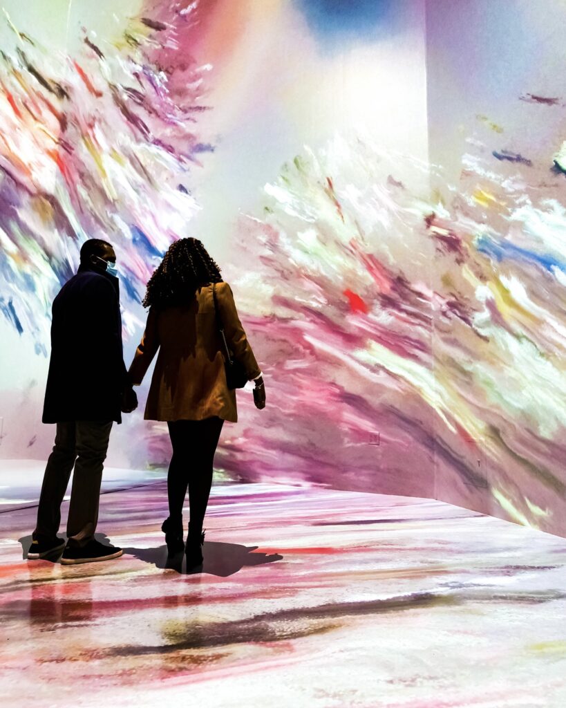 Couple holding hands for valentine's day walking in an immersive gallery space, full of color