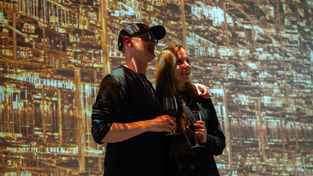 couple with cocktails and wine in immersive area with David Ariel's art behind them, gazing in awe