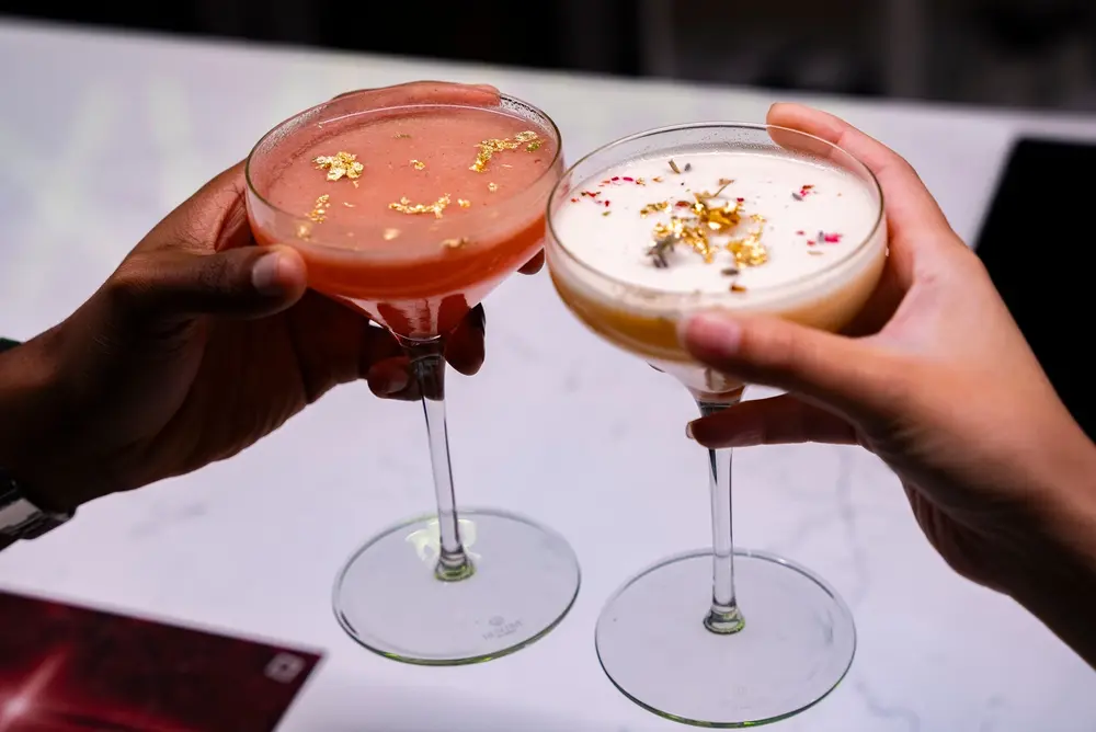 two people say cheers with a close up on beautiful, unique cocktails
